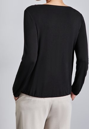 Top negro de manga larga con un escote amplio y una textura suave, visto desde atrás, combinado con pantalones beige claros.