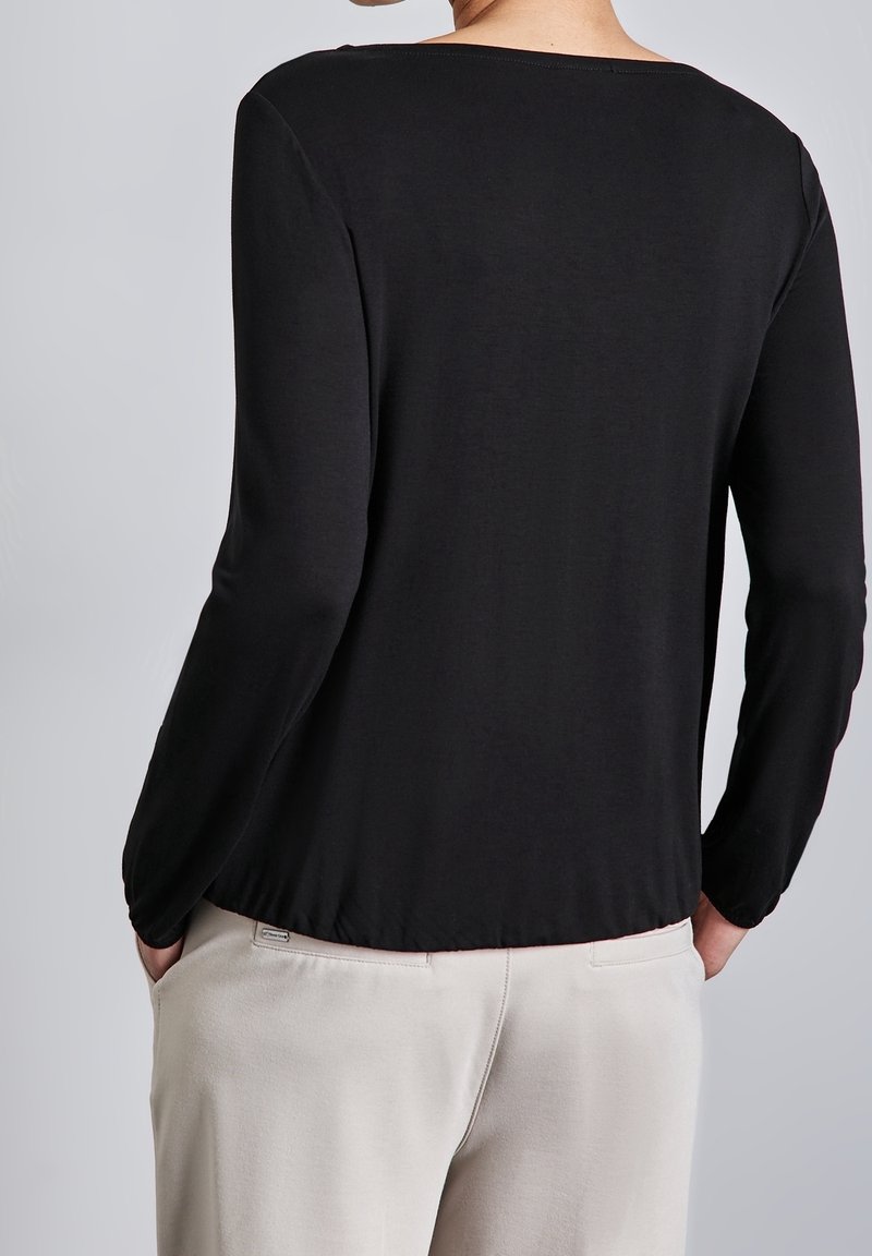 Svart långärmad topp med bred halsringning och slät textur, visad bakifrån, tillsammans med ljusbeiga byxor.