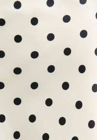 Tissu blanc avec de petits pois noirs espacés régulièrement formant un motif régulier.