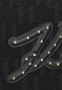 Zwarte textieltas met een gestructureerd patroon, omrand met een zwartleren logo versierd met gouden studs voor extra detail.