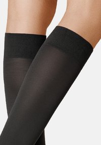 Schwarze blickdichte Kniestrümpfe mit einem strukturierten schwarzen Bündchen oben, gefertigt aus einem glatten, elastischen Material, das ein elegantes Erscheinungsbild bietet.