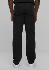 Pantalons noirs à jambes droites avec une texture lisse et des poches arrière, associés à des baskets blanches. Taille visible et finition soignée.