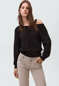 Suéter negro de punto con diseño de un solo hombro, dobladillo acanalado y mangas largas, combinado con jeans beige claros.