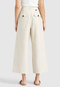 Crème wijde broek gemaakt van lichtgewicht stof, met twee achterzakken met knoopsluitingen en een rechte zoom.