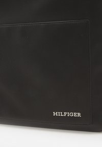 Borsa in tessuto nero con texture, dotata di una tasca piatta e del logo "HILFIGER" in argento. Presenta un design rettangolare elegante con bordi cuciti.