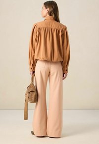 Chemise marron à manches bouffantes, associée à un pantalon large rose. Un sac texturé avec des trous est porté sur un côté.