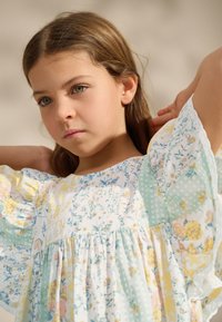 Leichtes Kleid mit Blumenmustern in Pastellfarben, mit Rüschenärmeln und einem gerafften, gestuften Design. Weiches, strukturiertes Material.