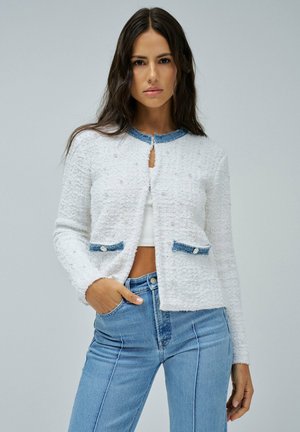Cárdigan blanco texturizado con detalles en denim azul, que presenta pequeñas embellishments similares a perlas y dos bolsillos frontales, cuello redondo y diseño corto.
