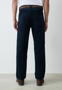 Navy corduroy pants with a straight leg cut, rear pockets, and a textured surface. Paired with brown footwear, viewed from the back.