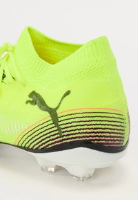 Crampon de football jaune néon avec une tige texturée, un motif de rayures noires et le logo Puma, featuring une semelle blanche avec des pointes transparentes.