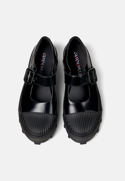 Chaussures en caoutchouc noires avec un bout arrondi, une sangle à boucle et une semelle striée. Surface lisse avec une finition mate et un motif coloré pour la semelle intérieure.