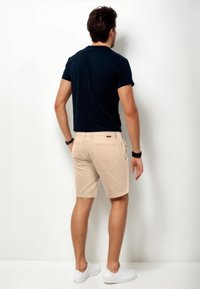 Beige Shorts mit strukturierter Oberfläche und zwei Gesäßtaschen, kombiniert mit einem dunkelblauen, eng anliegenden T-Shirt und weißen Sneakers.