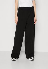 Pantaloni neri a gamba larga realizzati in tessuto morbido, con vita elasticizzata e cuciture laterali. Abbinati a sneakers con motivo.