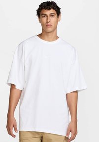 Camiseta blanca de gran tamaño hecha de algodón, con mangas cortas y un cuello redondo. Logo sutil en blanco en el pecho.