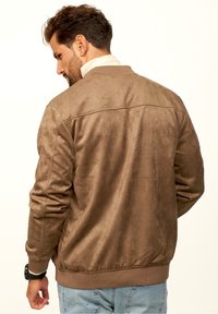 Braune Wildleder-Bomberjacke mit glatter Textur, gerippten Bündchen und Saum. Sie hat einen hohen Kragen und ein schlichtes Design ohne Verzierungen.