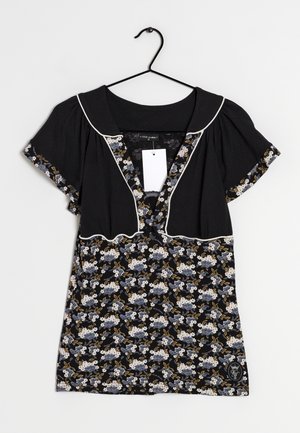 Blouse noire à manches courtes avec imprimé floral sur la moitié inférieure et les bordures des manches, passepoil blanc, col en V profond et une étiquette suspendue à l'intérieur du col.
