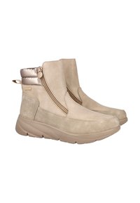 Botines beige con suelas gruesas, cremalleras laterales, material de ante suave, cuellos metálicos acolchados y tiradores en la parte posterior.