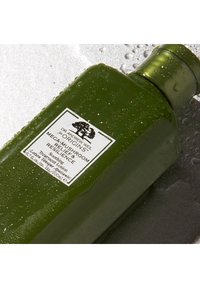 Grønn plastflaske med teksturert overflate, dråper av vann, hvit etikett som beskriver "Dr. Andrew Weil" og produktnavn. Skinnende kork.