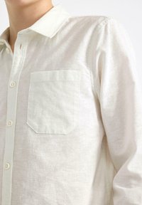 Jasny lniany koszula z kołnierzykiem zapinanym na guziki, z jedną kieszenią i strukturalnym materiałem, nadająca swobodny wygląd.