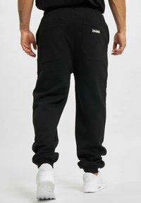 Schwarze Sweatpants mit einer lockeren Passform, ausgestattet mit zwei Gesäßtaschen, elastischen Bündchen und einem Logo-Accent auf der Gesäßtasche.