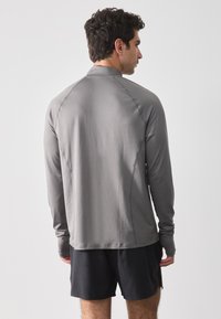 Lange mouw sportshirt in grijs, met een aansluitende pasvorm en een gladde textuur; voorzien van raglanmouwen en een ronde halslijn. Gecombineerd met zwarte shorts.
