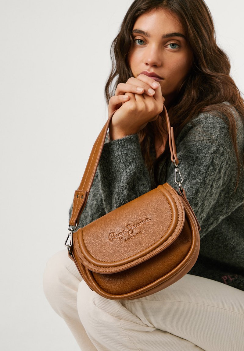 Brun läder crossbody-väska med en texturerad yta, rundad form och präglad logotyp. Utrustad med en avtagbar rem och metallisk hårdvara.