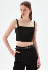 Top negro corto con escote cuadrado y tirantes finos; combinado con pantalones negros de cintura alta y un cinturón negro con hebilla plateada.