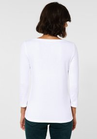 Witte langemouwen top met een ronde hals, een gladde textuur en een aansluitend ontwerp, gecombineerd met donkergroene jeans.