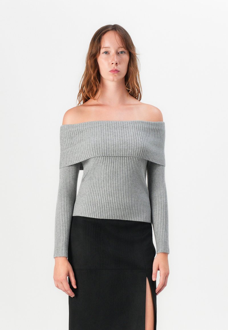 Grå ribbad off-shoulder tröja med långa ärmar, figurnära design och en kontrasterande svart kjol med en hög slits upp till låret.