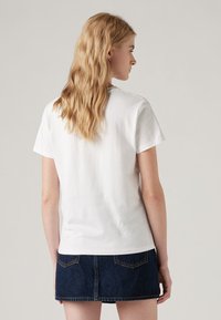 Camiseta de algodón blanca de manga corta y cuello redondo, combinada con una mini falda de mezclilla oscura. Textura suave y ajuste casual.