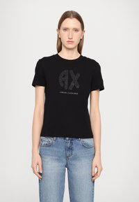 Černé bavlněné tričko s krátkými ruk�ávy, které má třpytivé logo "AX" a text "ARMANI EXCHANGE" pod ním. K tomu světlé modré džíny.