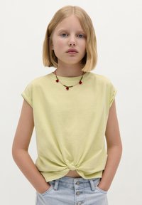 Limegrünes Kurzarm-T-Shirt mit einer Knoten-Detail vorne, kombiniert mit hellblauen, hoch taillierten Denim-Shorts.