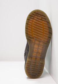 Chaussure noire avec une semelle en caoutchouc texturé. La semelle extérieure présente des rainures verticales et horizontales, offrant une meilleure adhérence. Un marquage notable est visible.