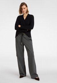 Czarny prążkowany sweter z dekoltem w serek, zestawiony z szarymi, szerokimi spodniami cargo z bocznymi kieszeniami i elastycznym paskiem w talii. Brązowe, spiczaste buty.