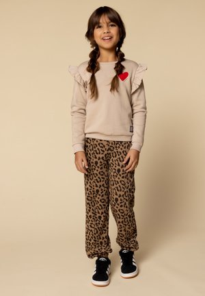 Beige sweatshirt met gerimpelde mouwen en een rood hart detail, gecombineerd met bruine panterprint broek en zwarte sneakers.