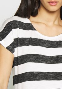 Černobílý pruhovaný top s krátkými rukávy, širokým výstřihem a texturovanou tkaninou, která zdůrazňuje kontrastní vodorovné linie.