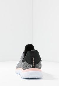 Black and gray knit shoe with a padded collar, pink outsole, and black heel tab. Features a textured upper and branded logo detail.