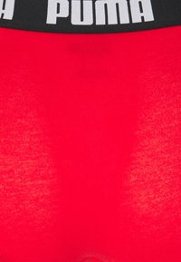 Rote Unterwäsche aus strukturiertem Stoff mit einem breiten schwarzen Bund, der vorne mit dem weißen "PUMA"-Logo bedruckt ist.