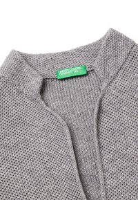 Suéter gris de punto con un patrón texturizado, que presenta un cuello doblado. La etiqueta dice "United Colors of Benetton" en verde.