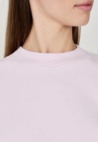 Jasnoróżowa bluza z okrągłym dekoltem o prążkowanym wykończeniu i gładkiej teksturze, prezentująca czyste linie i minimalistyczne detale wzornicze.