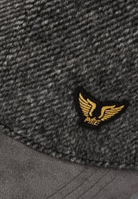 Tissu texturé gris foncé avec une petite pièce noire portant des ailes dorées et le mot "PINE" brodé en dessous.