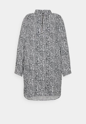 Langærmet tunika i sort og hvidt mønster med halv lynlås foran og opretstående krave, med let afrundet kant.