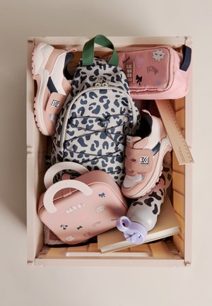 Różowo-białe dziecięce sneakersy, plecak w panterkę, różowy piórnik, linijka, butelka na wodę oraz różowy lunchbox w beżowej skrzyni.