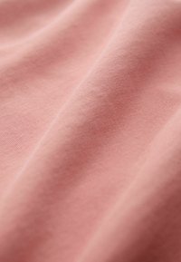 Pehmeä, sileä vaaleanpunainen kangas hienovaraisella tekstuurilla ja lempeillä laskoksilla, jotka luovat virtaavan pinnan.