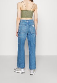 Löst sittande blå denimjeans med flera fickor, strukturerad tyg och en ljus tvätt, kombinerat med en metallisk grön crop top.