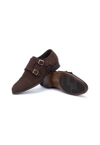 Zapatos de ante marrón con dos hebillas doradas, punta redondeada y tacón bajo. La suela de goma presenta un patrón texturizado para mayor agarre.