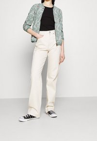 Ljusgrön bomberjacka med blommönster, svart T-shirt, gräddvita vida byxor och svarta sneakers med vita sulor.