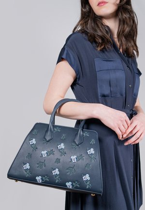 Sac en cuir marine avec broderie florale, texture lisse, forme structurée, double poignées et accents matériels visibles.