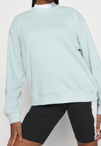 Ljusblå sweatshirt med rund halsringning, långa ärmar och ribbade muddar. Mjukt tyg med oversized passform, kombinerad med svarta shorts.