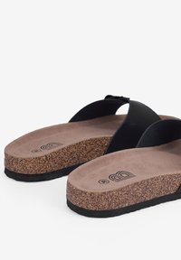 Sandales noires à glissière avec semelle en liège et rembourrage texturé marron. Dotées de larges lanières et d'une semelle en caoutchouc au design motif.